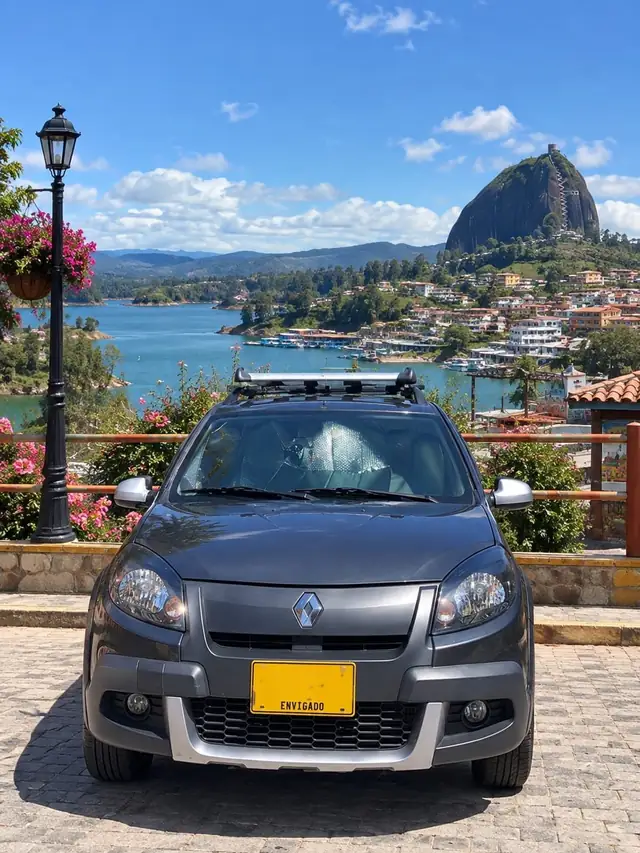 Renault Sandero gris oscuro de Latidos Tours, de frente, con barras de techo, junto al embalse de Guatapé